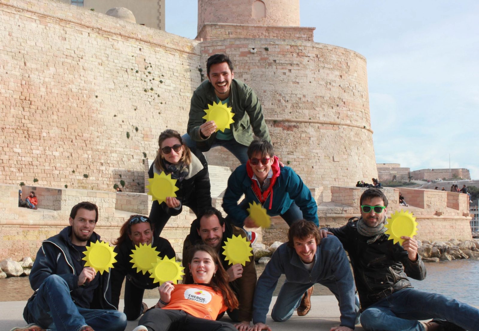 Une dizaine de membres du collectif, soleils en carton à la main, en pyramide devant des remparts, au bord de la mer